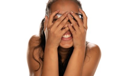 Mutlu ve utangaç, siyah tenli, beyaz arka planda gözlüklü bir kadın.