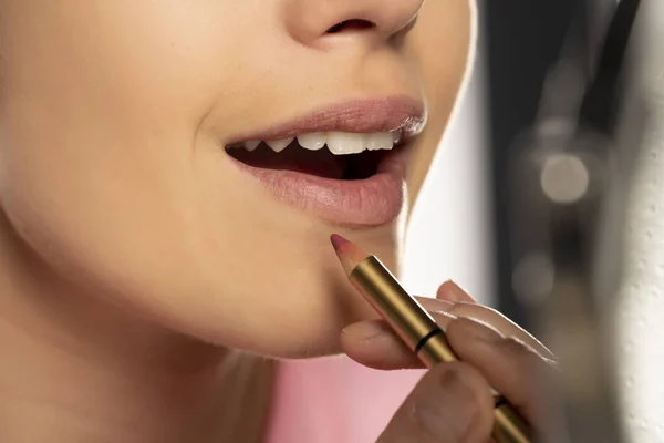 Young woman applying lip pencil on her lips on white background