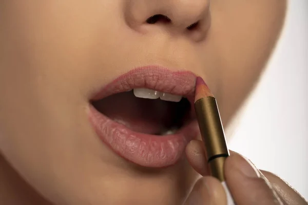 Young woman applying lip pencil on her lips on white background