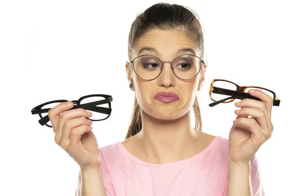 若い困惑した女性が白い背景に新しい眼鏡の枠を選び — ストック写真