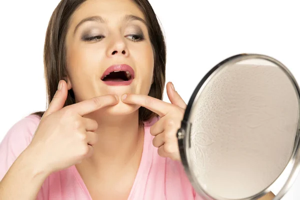 年轻女人在镜子的白色背景下挤压着她的粉刺 — 图库照片