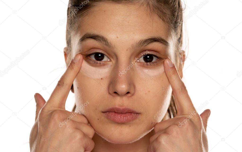 Portrait of young beautiful woman applying concealer with her fingers on white background