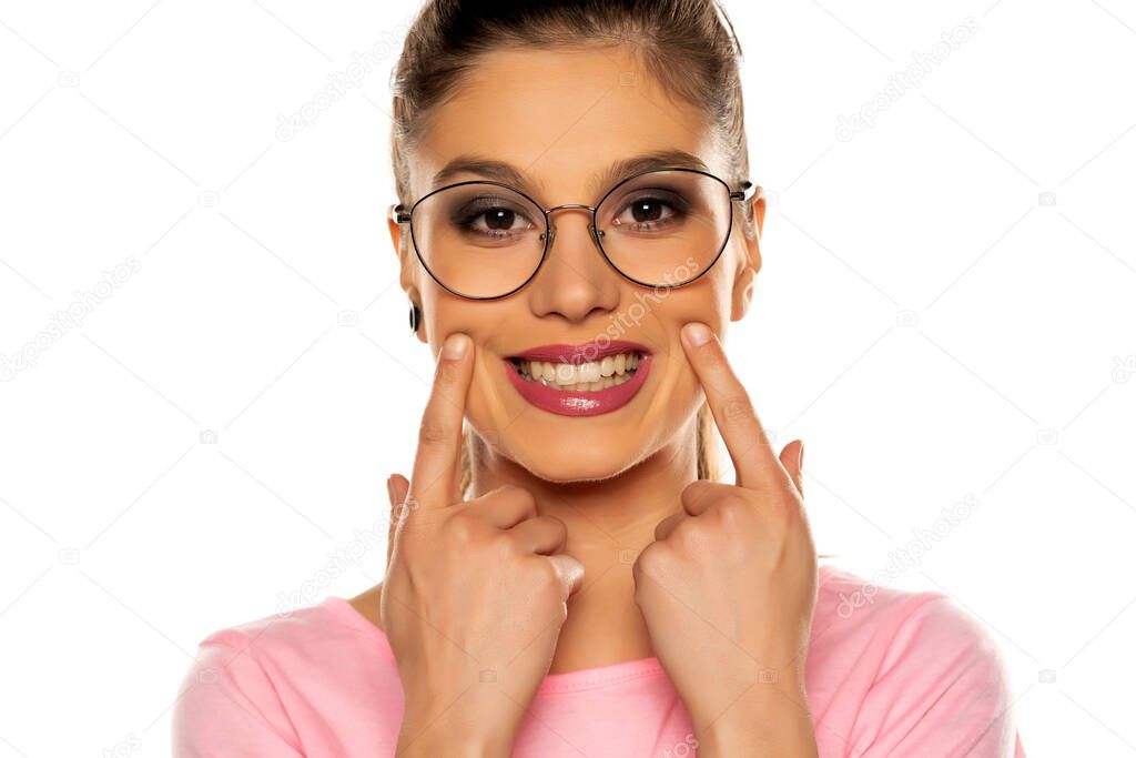 Portrait of young beautiful woman forcing her smile with her fingers on white background