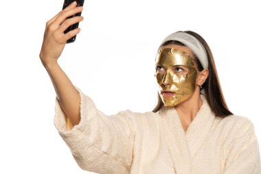 Genç kadın, beyaz arka planda altın maskeli selfie çekiyor.