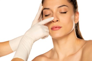 Doktorun elleri eldivenli beyaz arka planda genç bir kadının yüzünü kontrol ediyor.