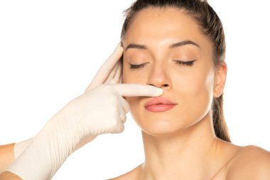 Eldivenli doktorun elleri beyaz arka plandaki genç kadının yüzünü kontrol ediyor.