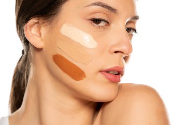 Beyaz arka planda yüzünde üç farklı sıvı fondöten tonu olan genç bir kadın.