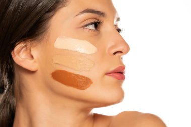 Beyaz arka planda yüzünde üç farklı sıvı fondöten tonu olan genç bir kadın.