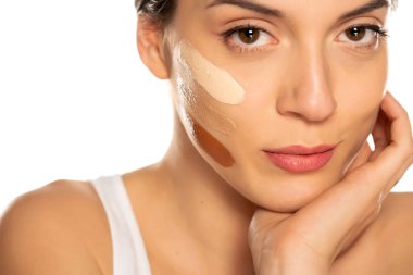 Beyaz arka planda yüzünde üç farklı sıvı fondöten tonu olan genç bir kadın.