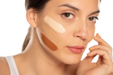 Beyaz arka planda yüzünde üç farklı sıvı fondöten tonu olan genç bir kadın.