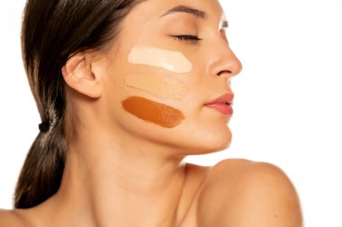 Beyaz arka planda yüzünde üç farklı sıvı fondöten tonu olan genç bir kadın.