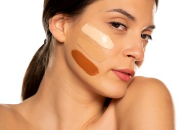 Beyaz arka planda yüzünde üç farklı sıvı fondöten tonu olan genç bir kadın.