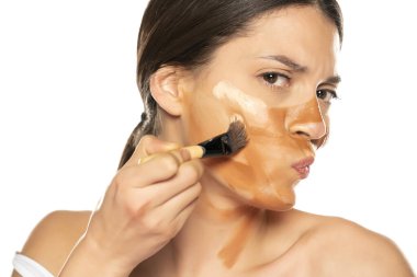 Genç sinirli kadın yüzüne üç farklı tonda sıvı fondöten sürüyor.