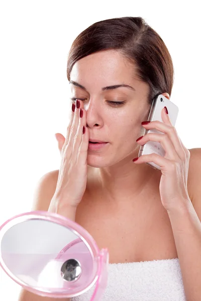 Mulher aplicando creme facial e falando ao telefone — Fotografia de Stock