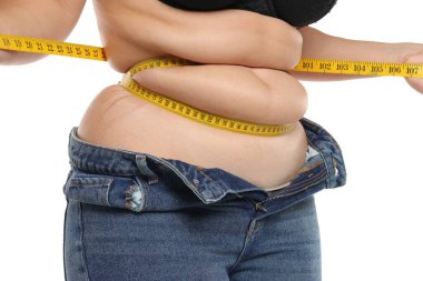 Obez kadınların göbeğine yakın stüdyo. Bant ve beyaz arka planda düğmesiz kot pantolon ile sıkılmış yağ kıvrımları..