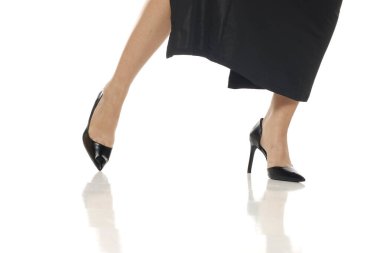 Stüdyo çekimlerinde kadın bacakları siyah topuklu ayakkabılar ve siyah elbiseler içinde yürür ya da beyaz arka planda poz verir..