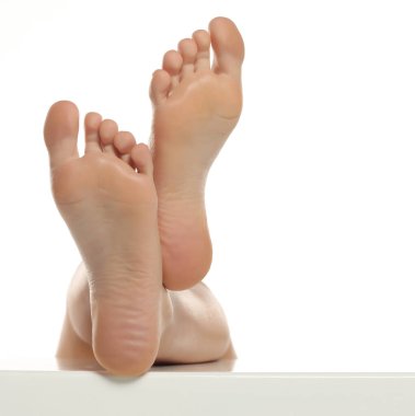 Bir kadının çıplak ayaklarının yükselişini ve hafifçe çapraz duruşunu, beyaz arka planda çekilen stüdyo çekimlerini, pürüzsüz ciltli tabanları gösteriyor.