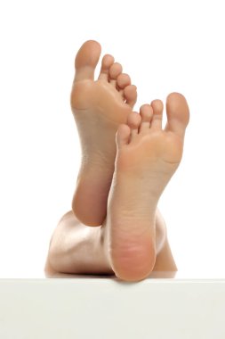 Bir kadının arka görüntüsü çıplak ayakla yükselir ve hafifçe çaprazlanır. Tabanları pürüzsüz görünür. Beyaz bir arka planda stüdyo çekimi..