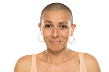 Askılı tişörtlü, kel bir kadının, doğal görünüşü ve beyaz arka planda hafif bir gülümseme.