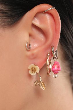 Beyaz arka planda altın bir çiçek, pembe boncuk ve gümüş piercing de dahil olmak üzere birden fazla küpeli bir kadının stüdyo yakın çekimi..