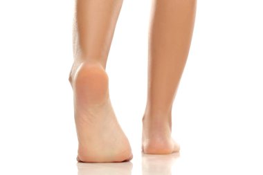 Kadın bacaklarının ve ayaklarının arka görüntüsü tabanları gösteriyor, parmak uçlarında pürüzsüz deri, beyaz arka planda stüdyo çekimi.