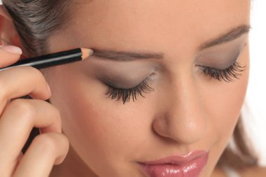 Kapalı gözlü, kaşlarını kalemle şekillendiren, beyaz arka planda stüdyo fotoğrafı olan bir kadının yakın çekimi..