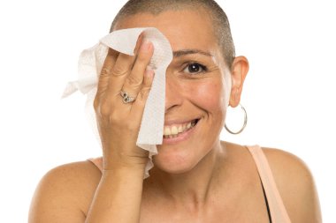 Beyaz arka planda gözüne mendil tutarken gülümseyen kel bir kadının stüdyo fotoğrafı.