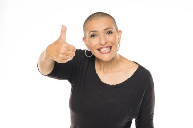 Siyah kıyafetli, gülümseyen ve beyaz arka planda baş parmak gösteren kel bir kadının stüdyo fotoğrafı.