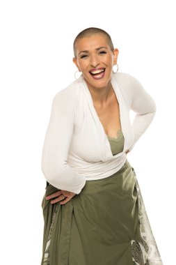 Saçları kazınmış, beyaz bluzlu, yeşil etekli, beyaz arka planda öne doğru eğilmiş gülümseyen bir kadının stüdyo fotoğrafı..