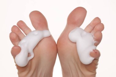 Ayak parmaklarına köpük sürmüş çıplak ayaklı bir kadının yakın çekimi, ayak bakım ve hijyen konsepti, beyaz arka planda stüdyo çekimi.