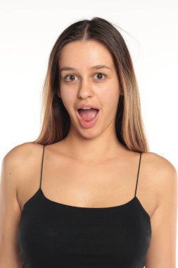 Stüdyo resmi, uzun siyah saçlı, siyah bluzlu, şaşırmış bir ifade takınan, beyaz arka planda portre çizen doğal bir kadın..