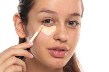 Gözlerinin altına kapatıcı süren genç bir kadın. Stüdyo beyaz bir arka planda..