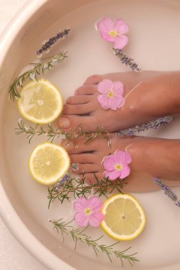 Doğal spa tedavisi için kadın ayaklarının limon dilimleri, biberiye, lavanta ve pembe çiçeklerle sırılsıklam olduğu bir stüdyo fotoğrafı.