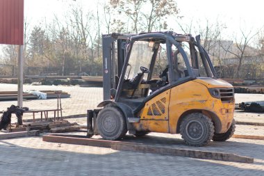Malzeme işlemleri sırasında metal depolama sahasında park etmiş endüstriyel bir forkliftin yan görüntüsü..