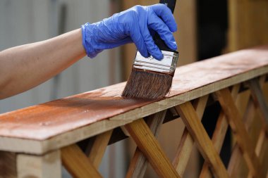 Mavi koruyucu eldiven giymiş, ahşap bir leke sürmüş, ahşap korkuluklara sürmüş..