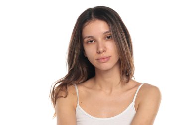 Beyaz bluzlu, makyajsız, sakin görünümlü esmer bir kadının beyaz arka planda portresi..