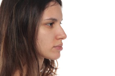 Tarafsız bir yüz ifadesi olan, makyajsız, beyaz bir arka planda stüdyo resmi olan genç bir kadının yan görünümü..