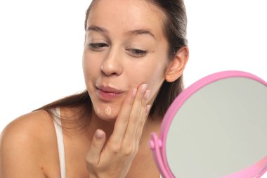 Çenesindeki temeli parmaklarıyla harmanlayan genç bir kadın, beyaz bir arka planda stüdyo çekimi..