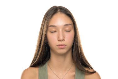 Uzun kahverengi saçlı, yeşil kolsuz tişörtlü, gözleri kapalı ve yüzü sakince beyaz arka planda genç bir kadının stüdyo fotoğrafı.