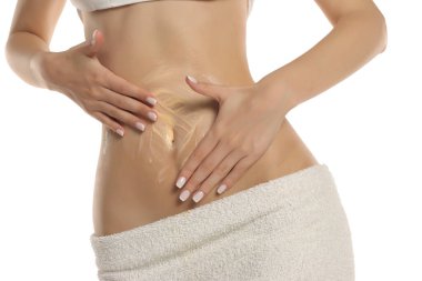 Beyaz bir arka planda beyaz bir havluya sarınıp karnına ve gövdesine kozmetik krem sürerken çekilmiş bir fotoğraf..