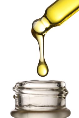 Beyaz arka planda açık bir cam şişenin üzerinde asılı duran altın kozmetik yağlı cam bir pipetin stüdyo çekimi..