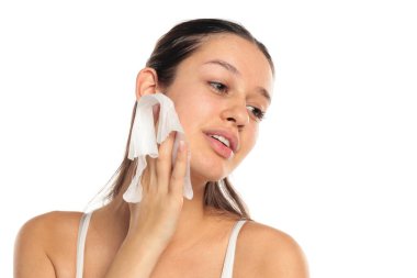 Uzun siyah saçlı, genç, şehvetli bir kadın yüzünü silip temizliyor. Beyaz bir arka planda stüdyo resmi..