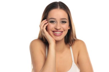 Uzun kahverengi saçlı ve makyajlı, beyaz bluzlu, beyaz bir arka planda çenesini dinlendirirken çekilmiş samimi bir gülümseme..