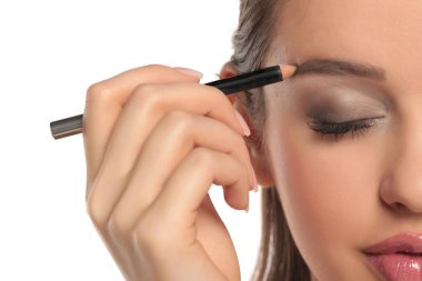 Kapalı gözlü, beyaz arka planda bir kalemle kaşlarını şekillendiren bir kadının yarım yüzünün stüdyo fotoğrafı..