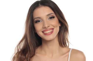 Makyajlı, gülümseyen esmer bir kadının beyaz bir arka planda doğrudan kameraya, portreye ve vesikalığa baktığı bir fotoğraf..