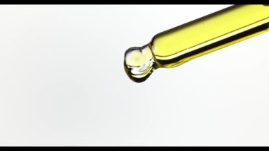 Altın kozmetik yağının beyaz arka planda cam bir pipetten damlayan yavaş çekim videosu