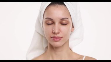 4k video, yavaş çekim, kafasında havlu olmayan, makyajsız genç bir kadının stüdyo çekimi, gözleri kapalı ve beyaz bir arka planda gülümsüyor..