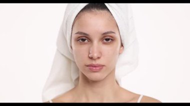 4k video, yavaş çekim, kafasında havlu olmayan, makyajsız genç bir kadının stüdyo çekimi, gözleri kapalı ve beyaz bir arka planda gülümsüyor..