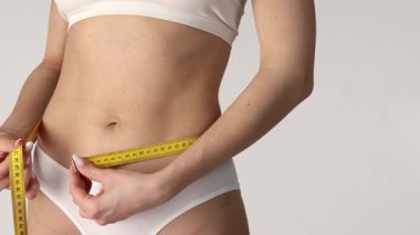 Belini mezurayla ölçen bir kadının ön görüntüsü ve baş parmak hareketi, sağlık ve zindelik konsepti, beyaz arka planda stüdyo çekimi, 4K