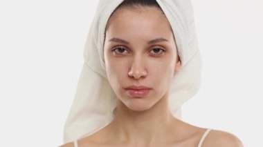 4k video, kafasında havlu olan ve makyajsız genç bir kadının beyaz arka planda gülümsemeden, cilt bakımına ve hijyen anlayışına geçişi..